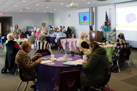  Becki Doiron stands at a podium and addresses a room full of seniors sharing information about brain and body health.