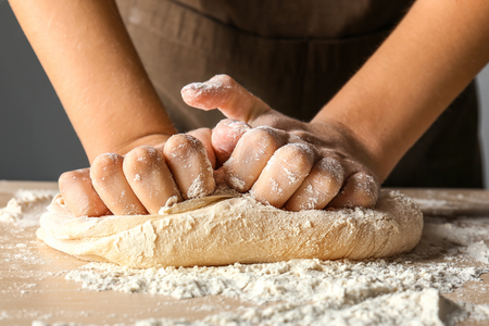 Two hands kneading bread dough on a cutting board with flour