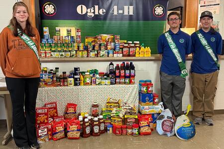 Three youth standing with food and Ogle County 4-H banner