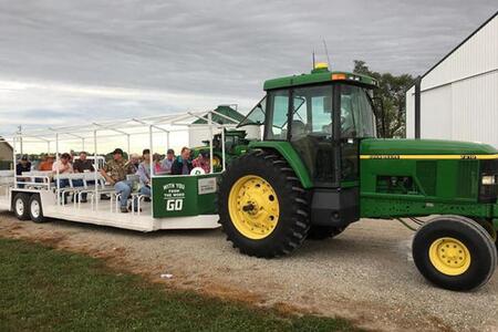 A green tractor pulls a seated trailer full of people around a farm tour 