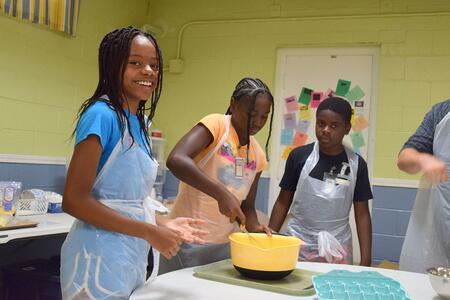 three kids stirring something in a yellow bowl