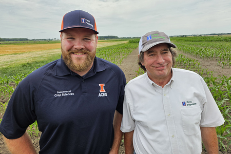 Two crops researchers pose smiling at the camera while standing in a corn field