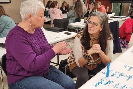 two women sitting at a table talking to each other