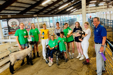 Group of people in green 4-H shirts with animals and news reporters