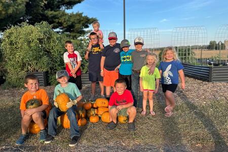 Learn Grow Share 4-H Club members posing as a group, some sitting on pumpkins or holding a pumpkin