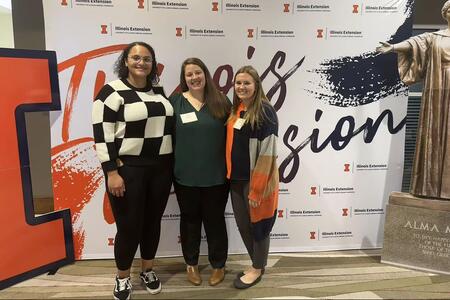 Vanessa Jones, Emily Harmon, and Rachel Mannen standing in front of Illinois Extension display