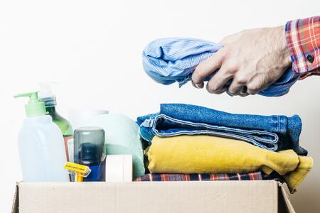  hands adding clothes to a box of clothes and personal items