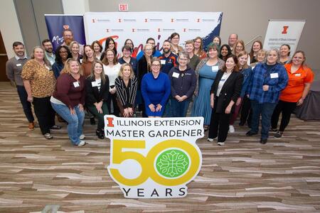 A group of people in front of a sign that says 50 years Illinois Extension Master Gardener