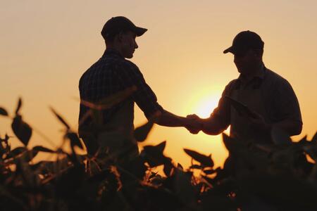 Two farmers talk on the field, then shake hands.