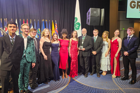 Delegates in formal wear pose in front of curtains.