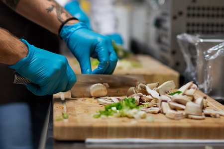 Person slicing vegetables on a cutting board in a professional kitchen.