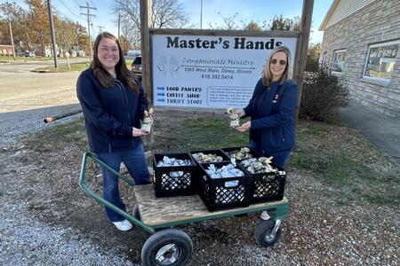 Extension staff holding packages of ground venison next to a cart with crates of venison and a local food pantry sign