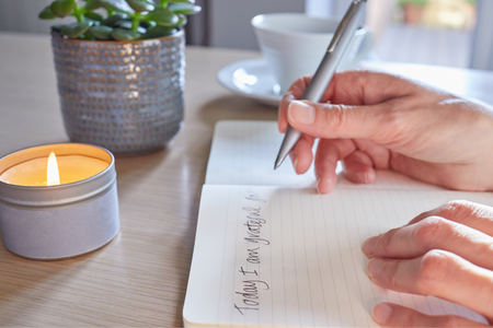 Person journaling in a notebook on a table by a candle