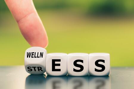 A finger flipping a block that says "welln" and "str" next to three more blocks that say "e, s, s" to spell wellness and stress