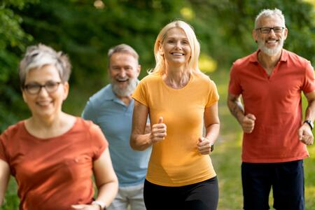 Four older adults jogging on a wooded trail.