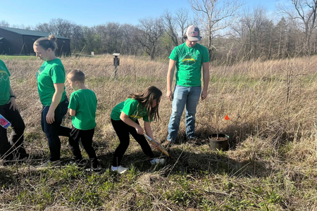 Youth in green shirts plant trees in a field. 