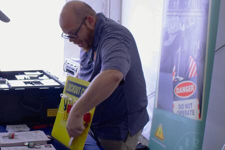 A person shows a lock and tag out bin safety system at an event table