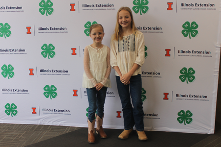Two youth stand in front of a 4-H and Illinois Extension step and repeat banner