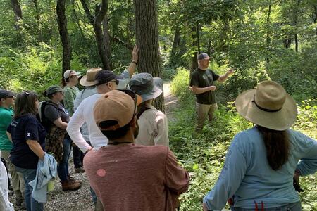 A group of people in the woods watch a man demonstrate something