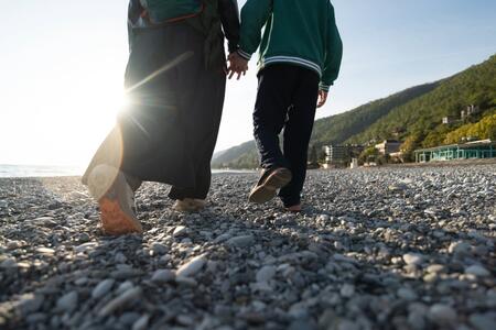 Two people walking on a rocky beach with the sunsetting in the background. 