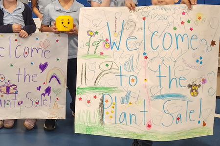 Students hold up signs that say "welcome to the plant sale"