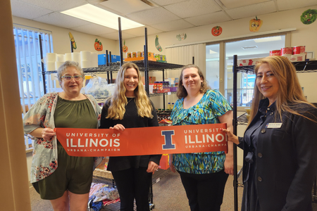Four people hold up a ribbon inside a food pantry room