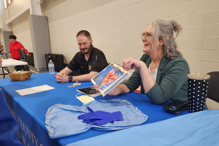 Two people sit at a table, showing images to a group of students