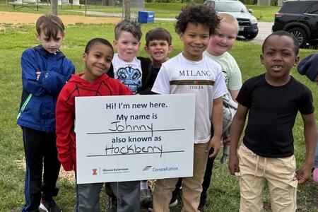 students pose in front of the sign of the tree they planted and named
