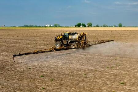 A sprayer traveling across a farm field releasing liquid herbicide. 