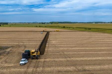 Overhead drone footage of a crew installing drainage pipe down the center of a farm field plot.