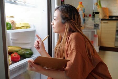 A woman with a clipboard checks the food in an open refrigerator