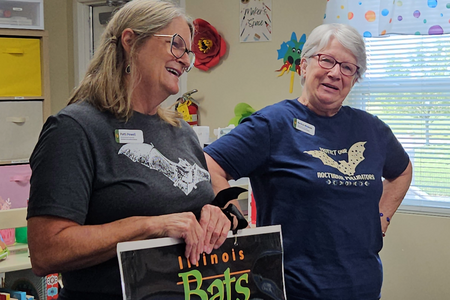 Patti Powell and Becki Wisdom holding Illinois Bats poster during a program