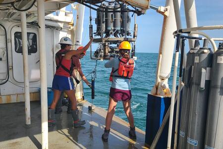 two women in hard hats use machinery on a boat in the ocean