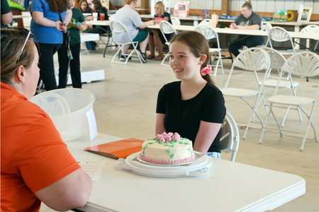 A 4-H'er happily presents her decorated cake for judging