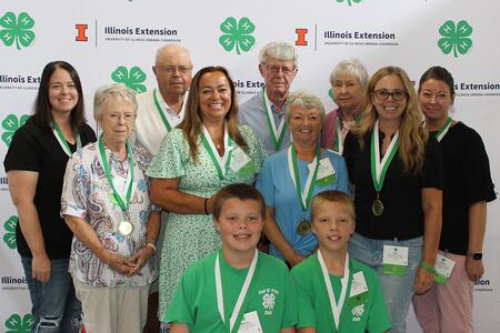 a smiling group standing in front of a 4-H backdrop