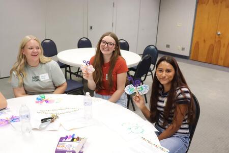 Three girls smiling for a picture with their coffee filter butterflies they made at Teen Teacher training.