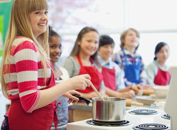 Youth smiling while stirring pot on stove at cooking class