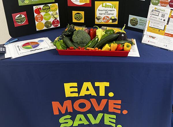 table with blue Eat. Move. Save. tablecloth and tray of fresh vegetables and nutrition education materials