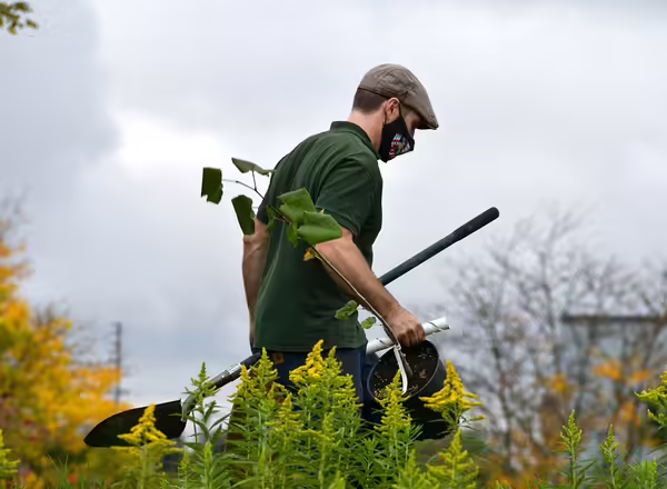a man in a green shirt holding a pair of gardening tools