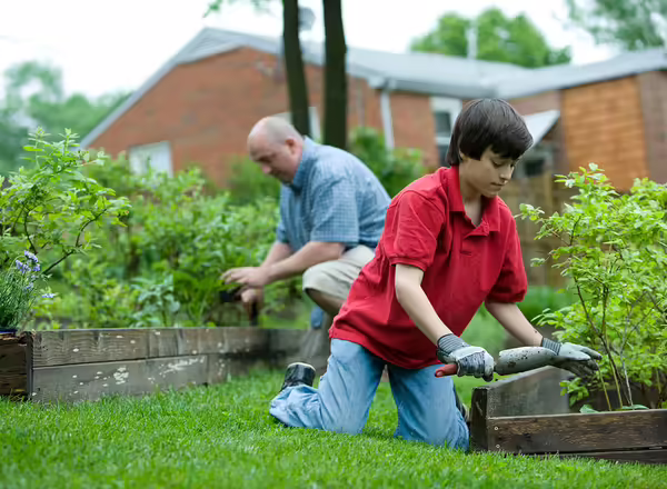 man in red polo shirt and blue denim jeans sitting on brown wooden bench during daytime