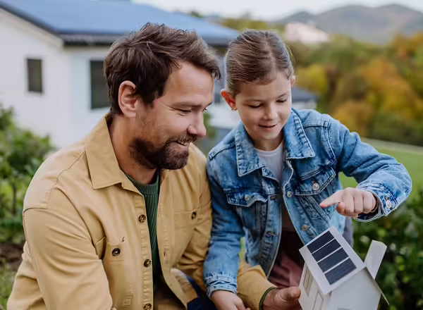 Little girl with her dad holding paper model of house with solar panels, explaining how it works.Alternative energy, saving resources and sustainable lifestyle concept. 