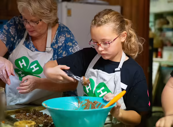 4-H Coordinator and youth mix candy in a large bowl.