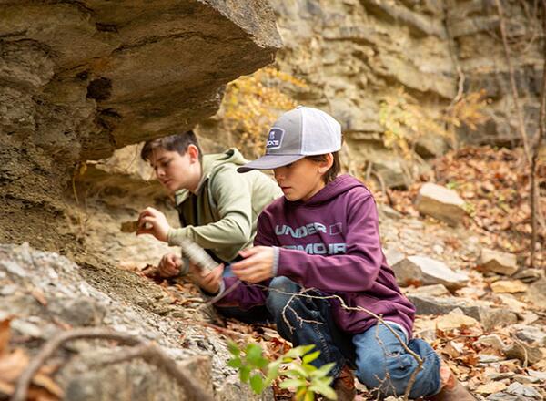 4-H youth explore a rock formation in the forest while fossil hunting. 