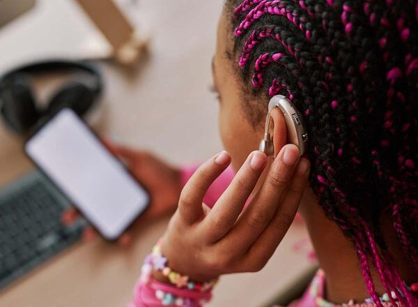 young girl with hearing aid looking at her phone 