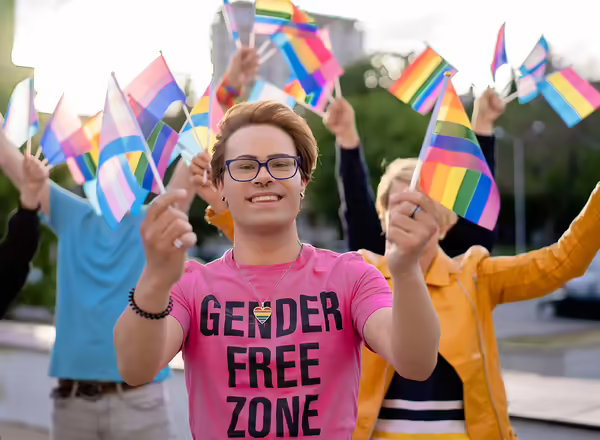 LGBTQ+ activist holding different flags of LGBTQI community defending the human rights, looking at camera