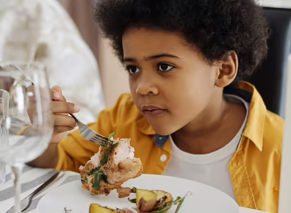 young boy eating chicken and baked potato