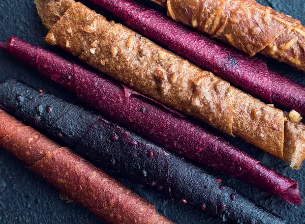 Sweet pureed fruit roll-up pastila. Homemade fruit leather of apple, apricot, strawberry and blueberry on black background. Fruit rolls. Dried fruits. Top view. Close-up.