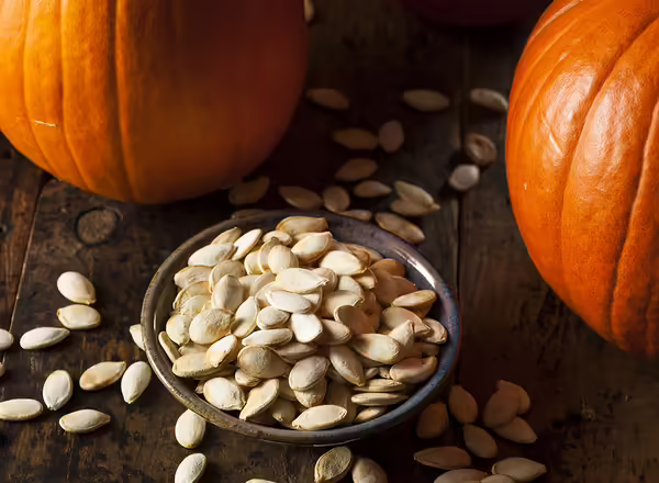 salted roasting pumpkin seeds on a table with 2 pumpkins