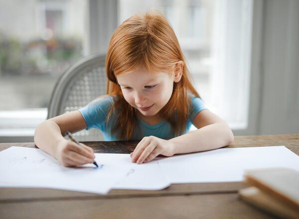 young girl writing with crayon in journal