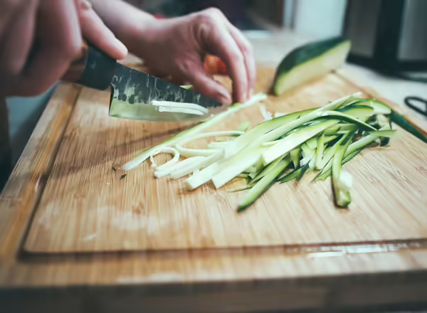 Hands of person slicing cucumber on wood cutting board